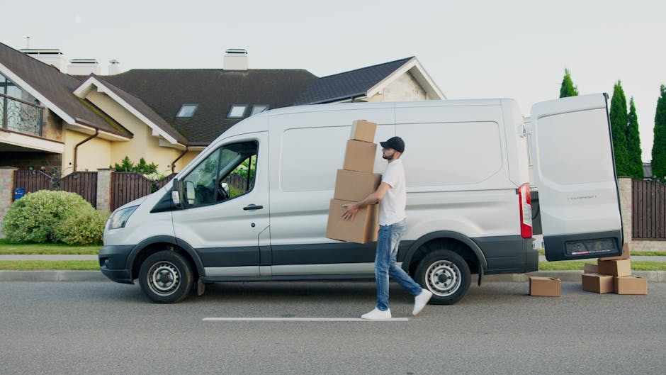 A curved cobblestone driveway with two white trucks parked side by side, partially visible behind a brick wall on the right. The trucks are positioned for a home relocation, with their cargo doors clo